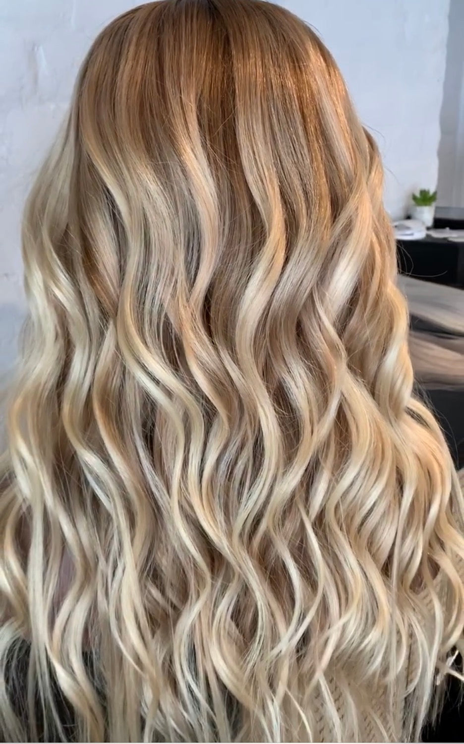 Model wearing a long, wavy, balayage brown to blonde wig.- Nuola Wigs